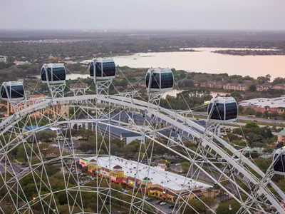 Several capsules of The Orlando Eye in the foreground with a lake in the background. The sun is also setting.
